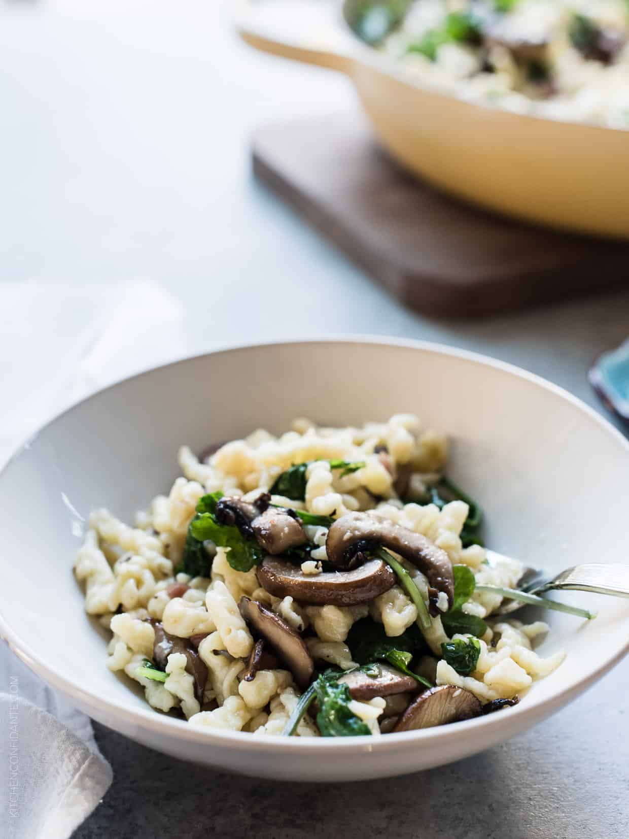 White bowl filled with Spaetzle with Garlic Butter Mushrooms and Baby Kale.
