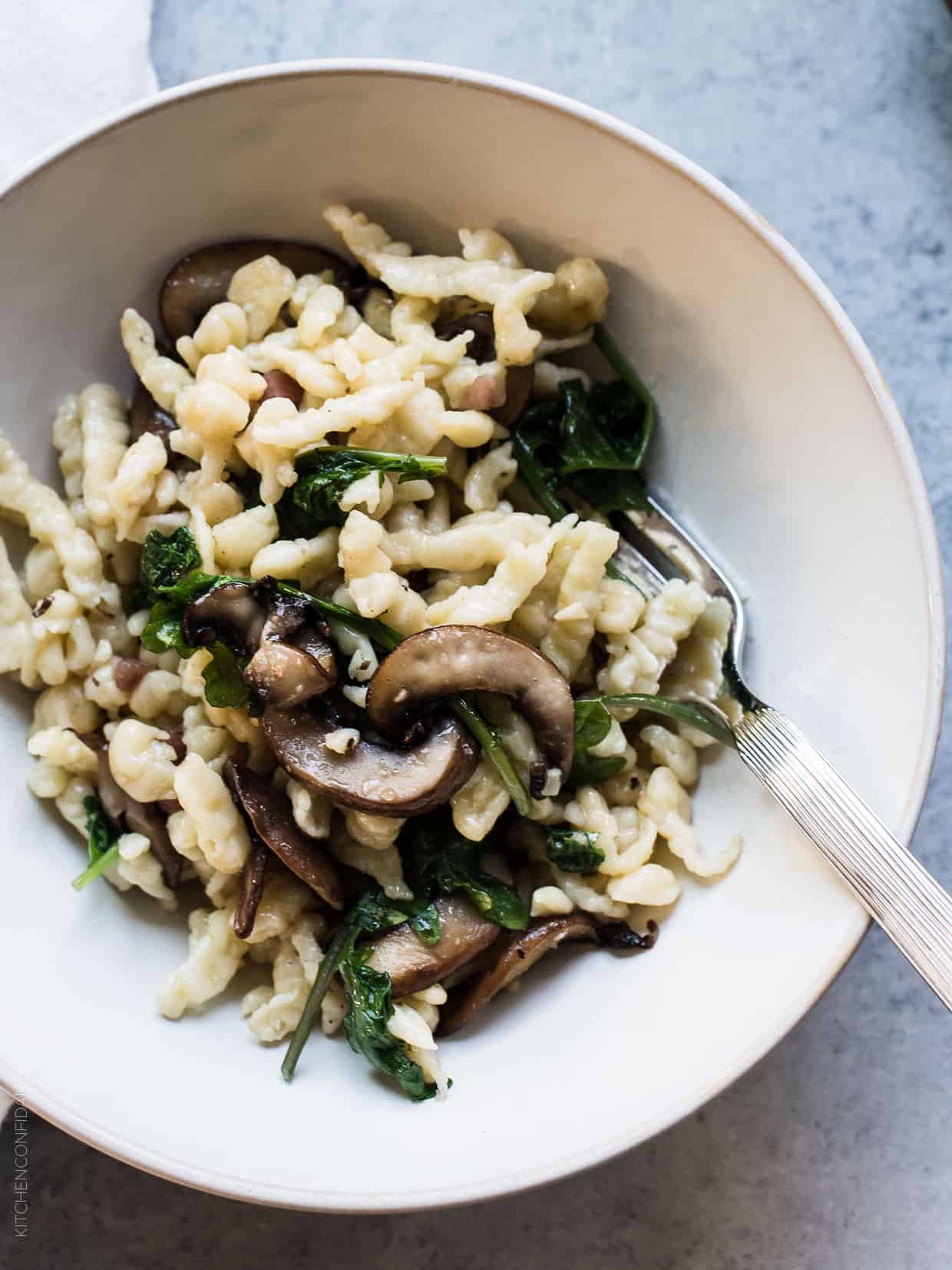 White bowl filled with Spaetzle with Garlic Butter Mushrooms and Baby Kale.