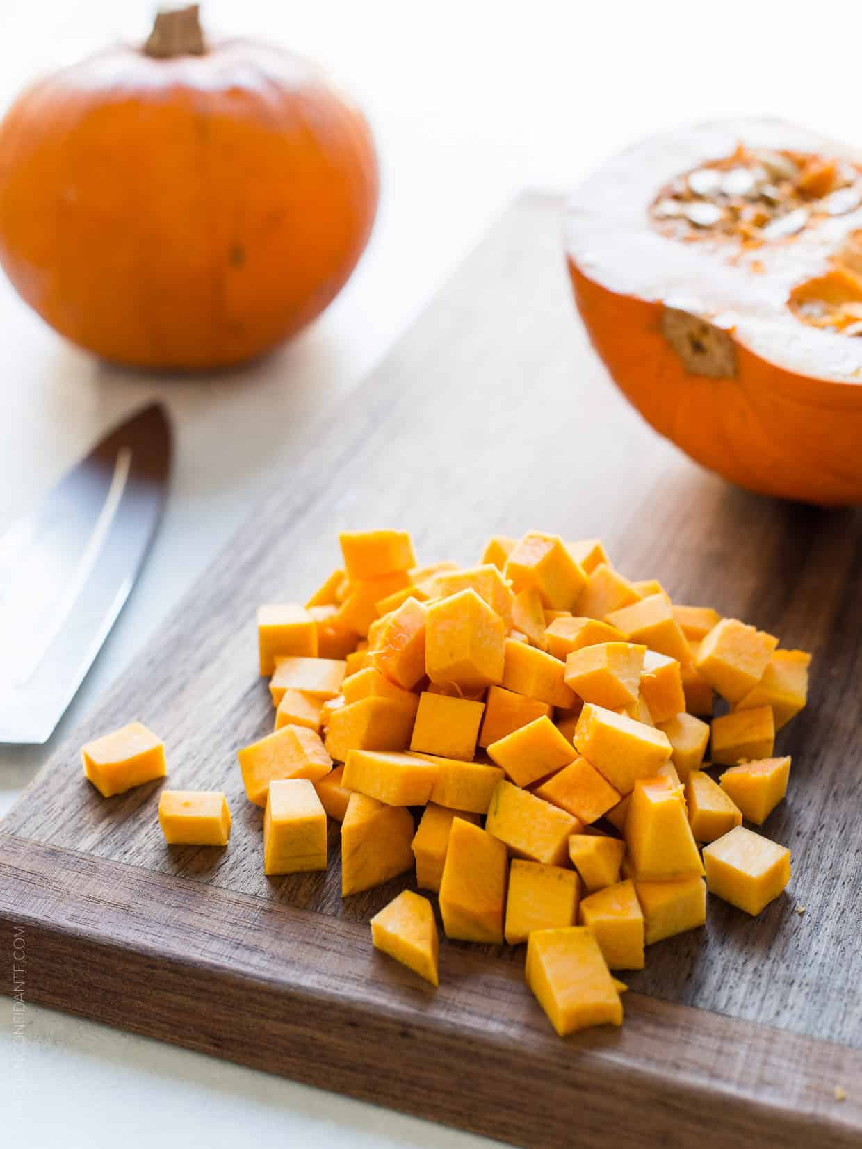 Diced pumpkin chunks on a wooden cutting board ready to be used in Turkey Pumpkin Pot Pie.