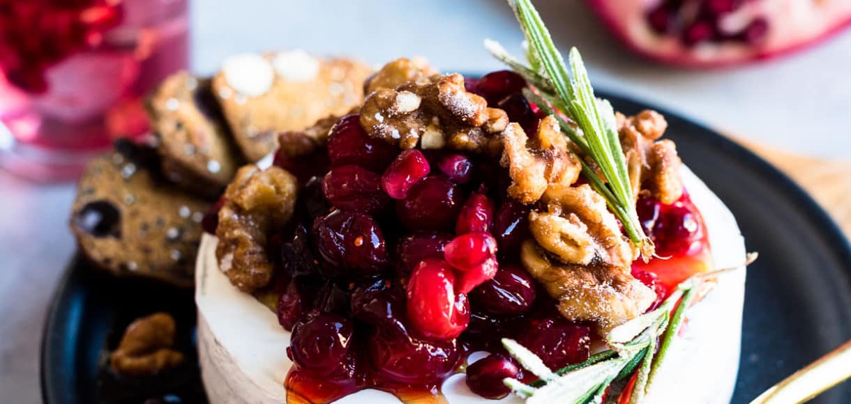 Cranberry Pomegranate Baked Brie served on a black plate with segments of fresh pomegranate in the background.