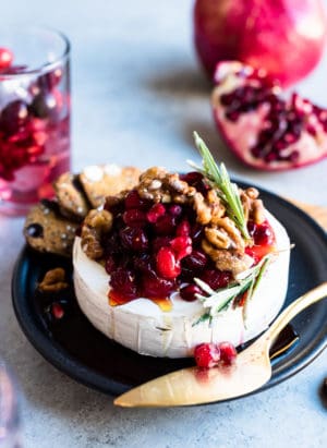 Cranberry Pomegranate Baked Brie served on a black plate with segments of fresh pomegranate in the background.