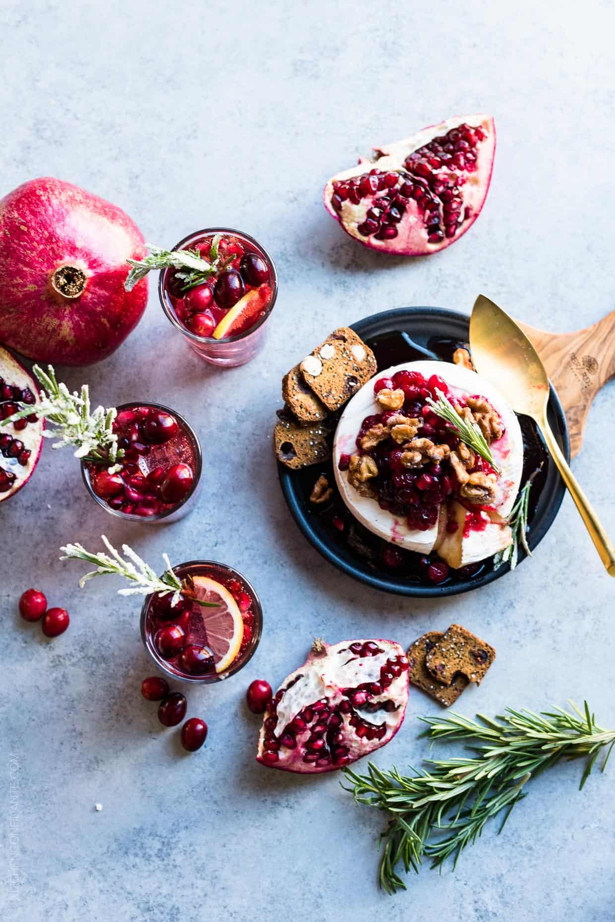 Cranberry Pomegranate Baked Brie served on a black plate with segments of fresh pomegranate and sprigs of rosemary in the background.