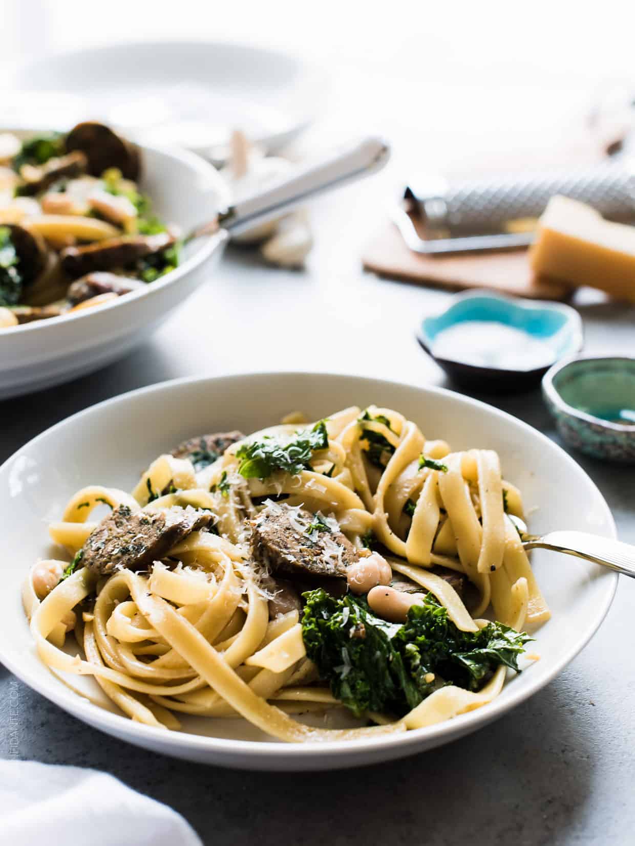 Fettuccine with Chicken Sausage, Kale and Cannellini Beans in a white bowl with the pasta twirled around a fork.
