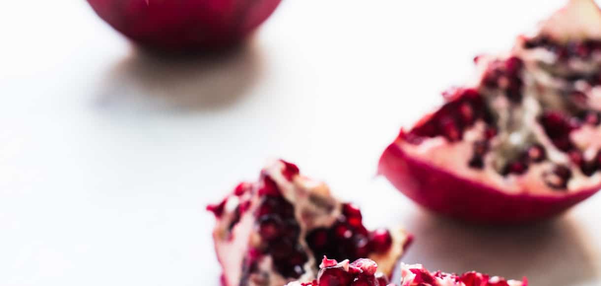 Pomegranate split into segments on a white surface.