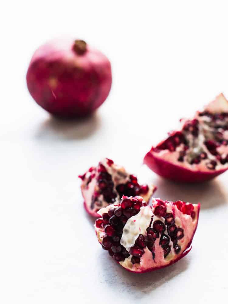 Pomegranate split into segments on a white surface.