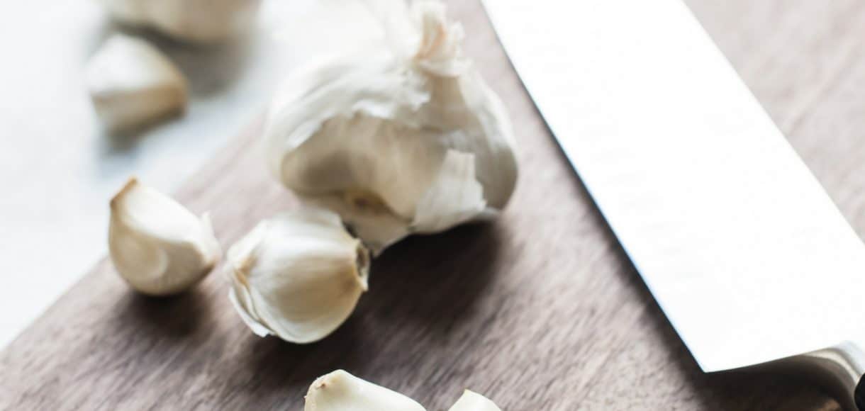 Garlic cloves and a knife on a wooden cutting board.