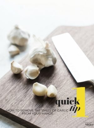 Garlic cloves and a knife on a wooden cutting board.