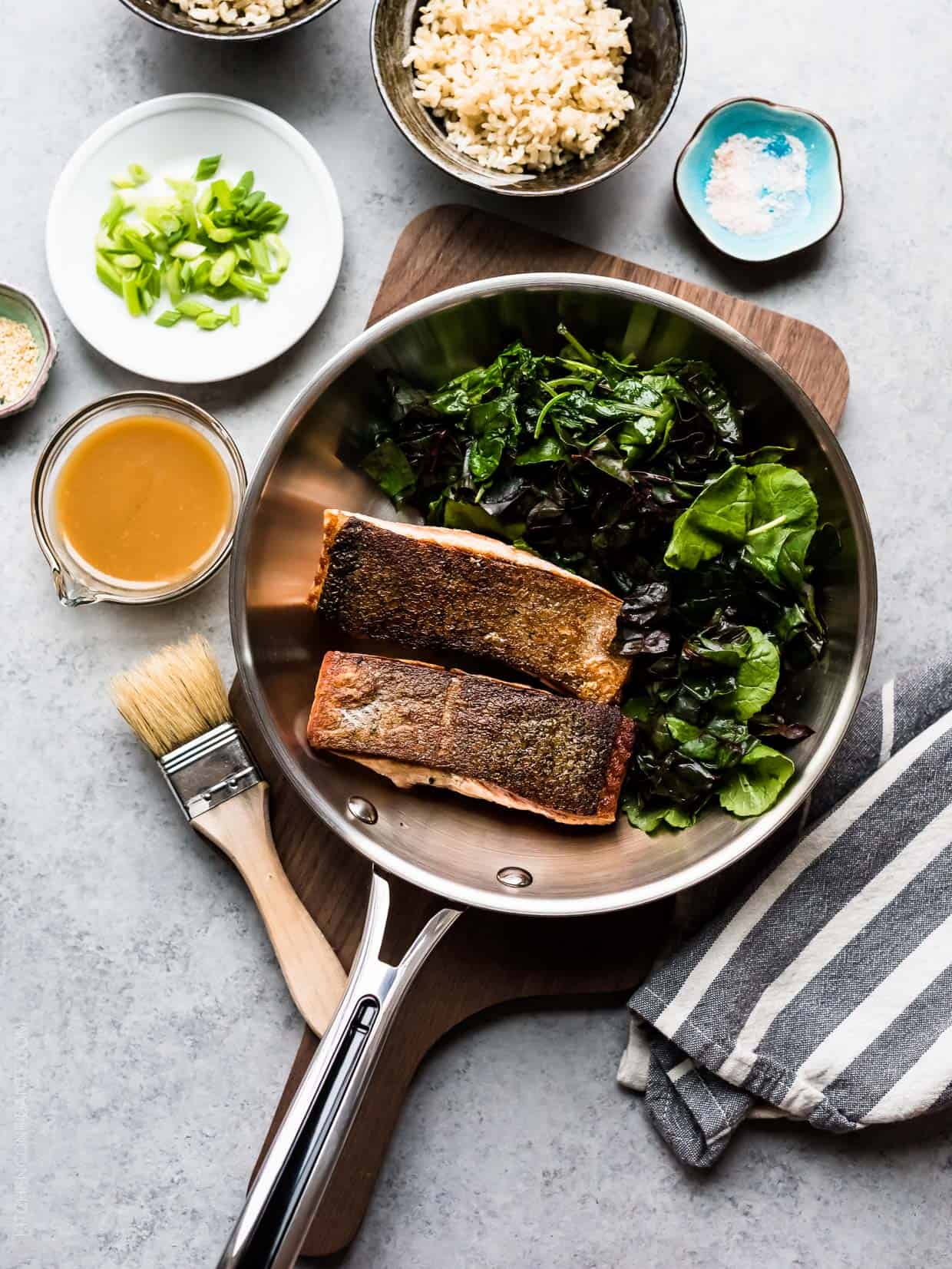 Miso Maple Glazed Salmon in Revere Cookware surrounded by a wilted green salad and additional ingredients.