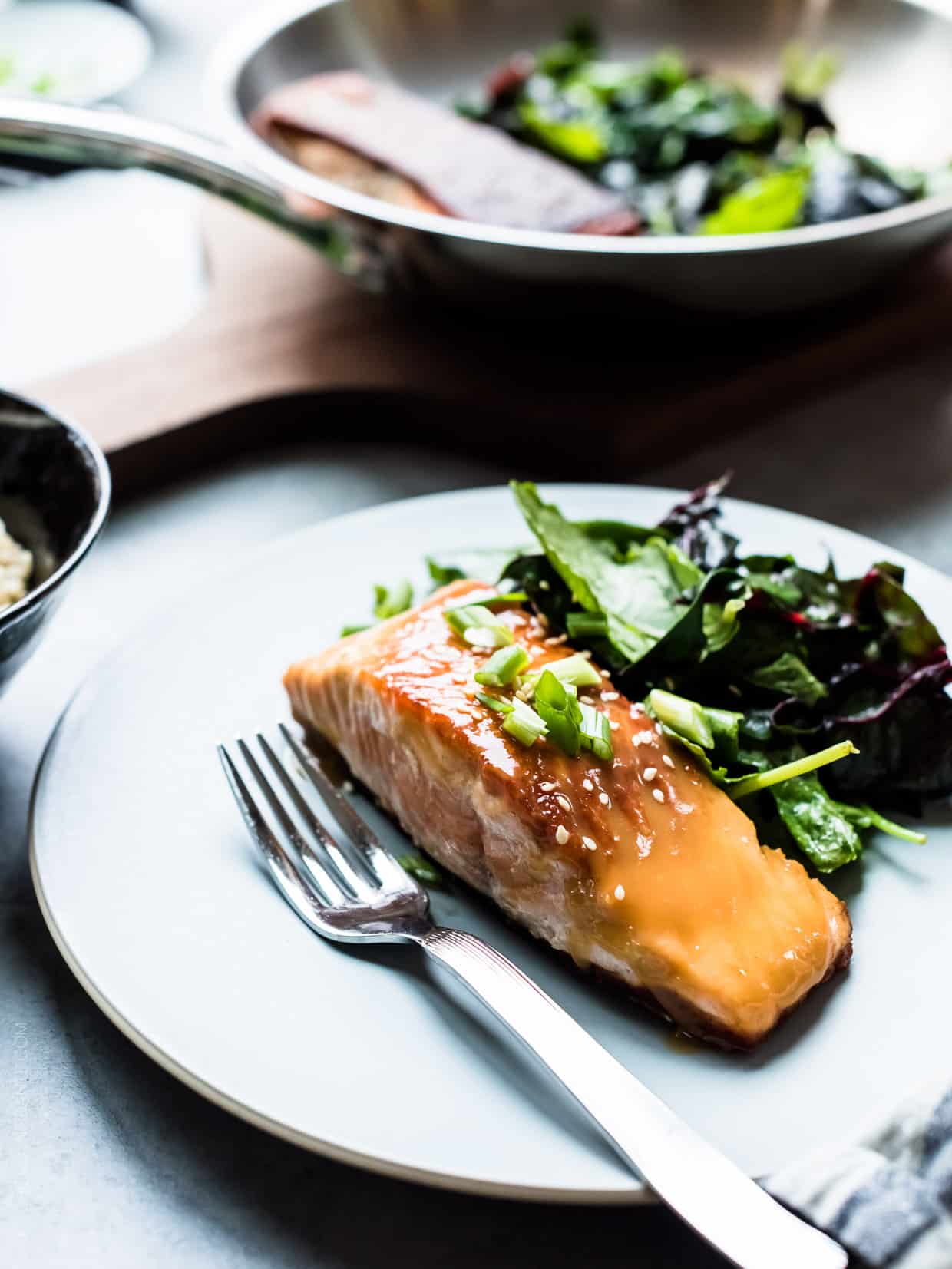 Miso Maple Glazed Salmon served on a white plate alongside a salad of wilted greens.