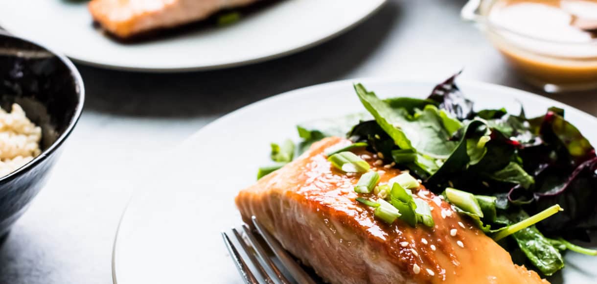 Miso Maple Glazed Salmon served on a white plate alongside a salad of wilted greens.