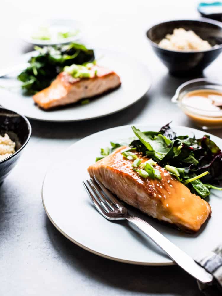 Miso Maple Glazed Salmon served on a white plate alongside a salad of wilted greens.