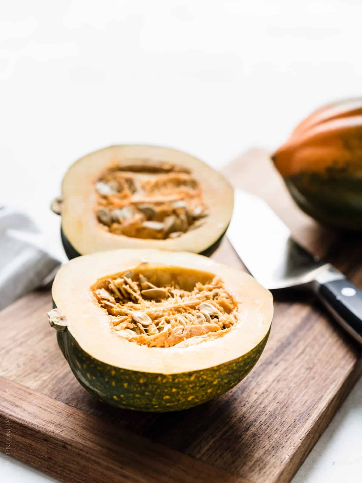 Acorn squash cut in half on a wooden cutting board with a chef's knife in the background.
