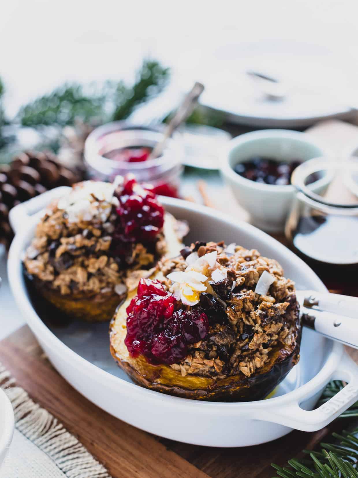 Two halves of Baked Oatmeal Stuffed Acorn Squash in a white baking dish garnished with cranberry sauce.