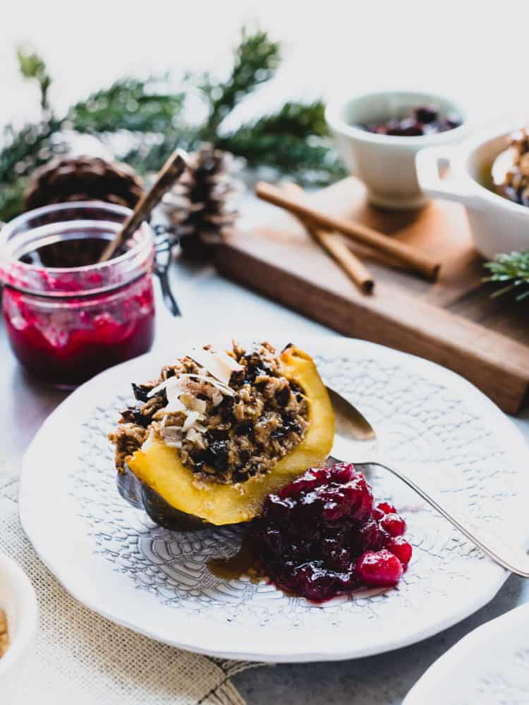 Wedge of Baked Oatmeal Stuffed Acorn Squash on a white plate served with cranberry sauce on the side.