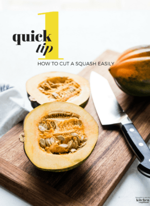 Acorn squash on a wooden cutting board cut in half with a chef's knife.