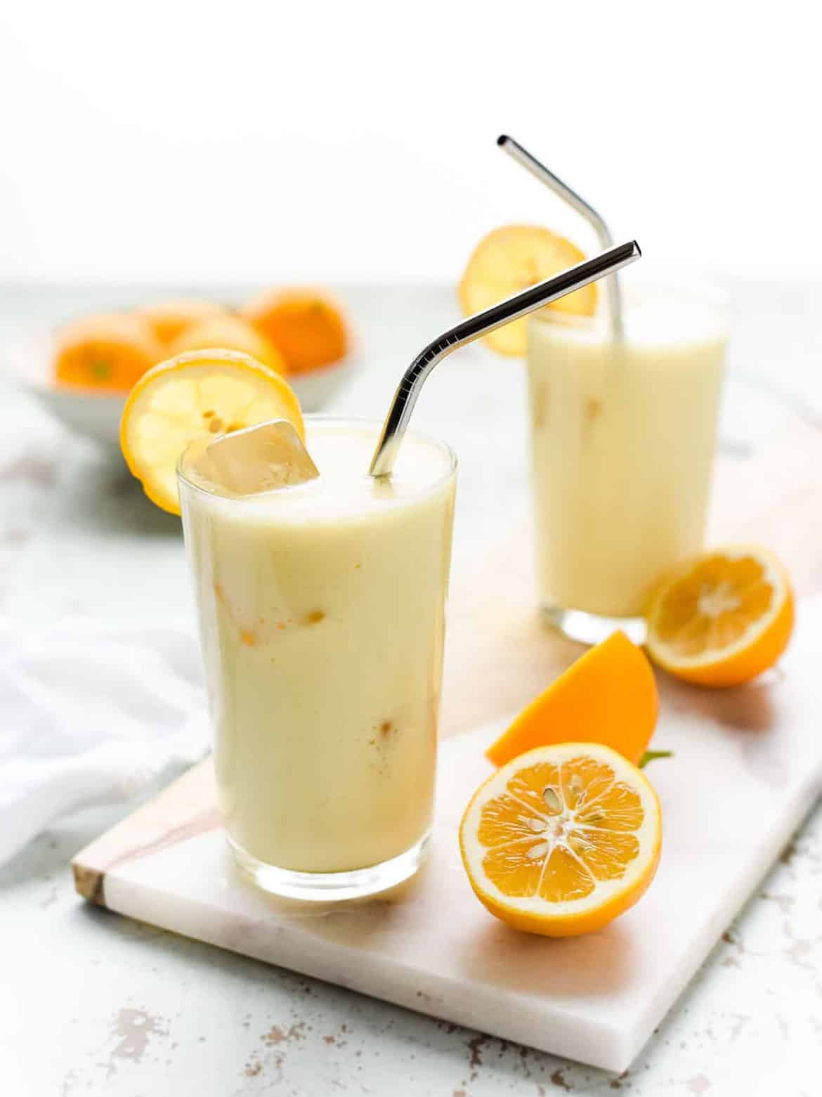 Meyer Lemon Honey Lassi in glasses with metal straws and halved oranges
