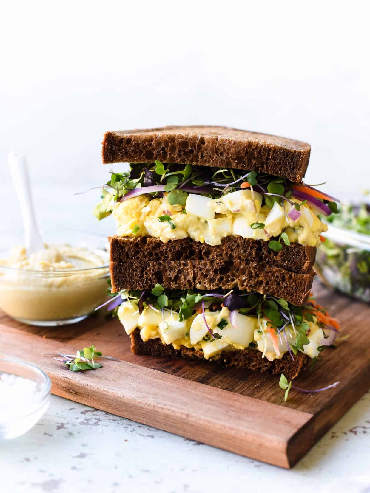 Hummus and Tahini Egg Salad stacked on a wooden board next to a bowl of hummus