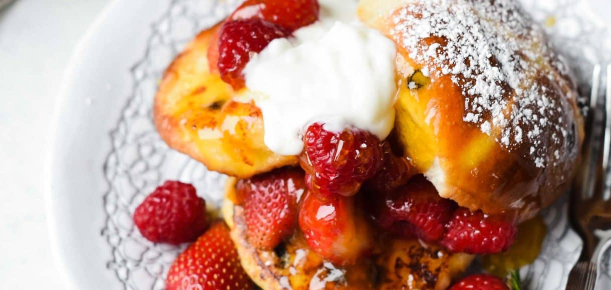 Hot Cross Bun Pain Perdu with fresh berries and cream on a white plate.