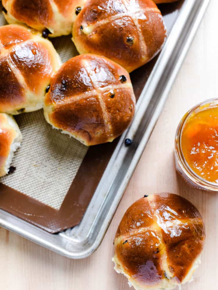 Homemade hot cross buns on a baking sheet.