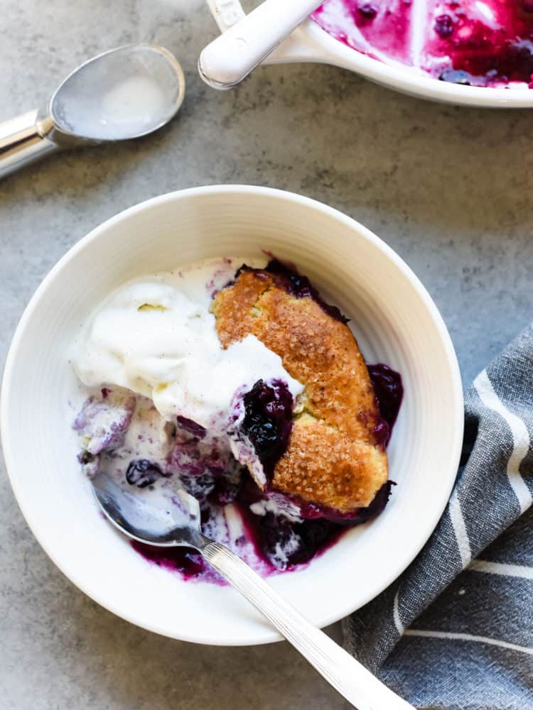 Blueberry Rhubarb Cobbler with melting vanilla ice cream in a white bowl.