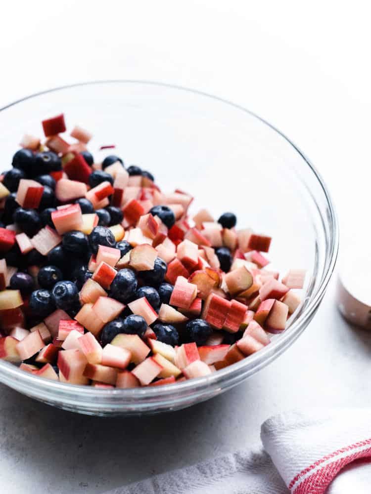 Blueberries and diced rhubarb in a glass bowl for a Blueberry Rhubarb Cobbler recipe.