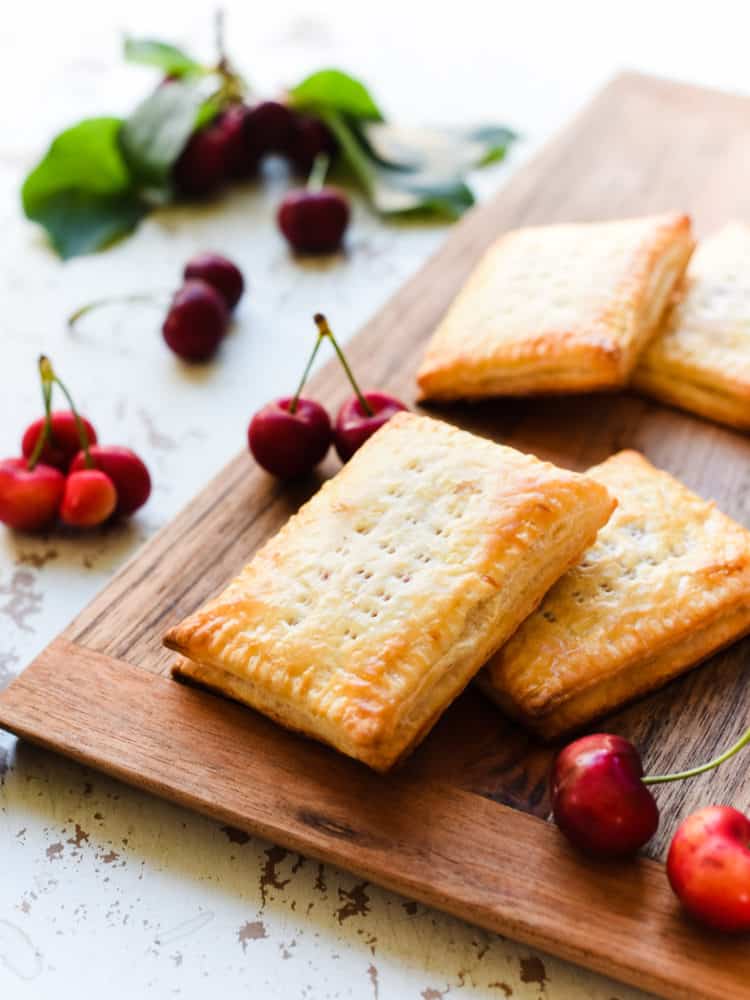 Homemade Cherry Pop Tarts without glaze on a wooden board with fresh cherries.