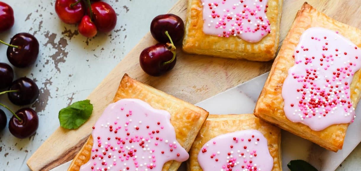 Homemade Cherry Pop Tarts on a wood and marble serving board with fresh cherries.