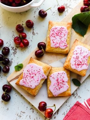 Homemade Cherry Pop Tarts on a wood and marble serving board with fresh cherries.