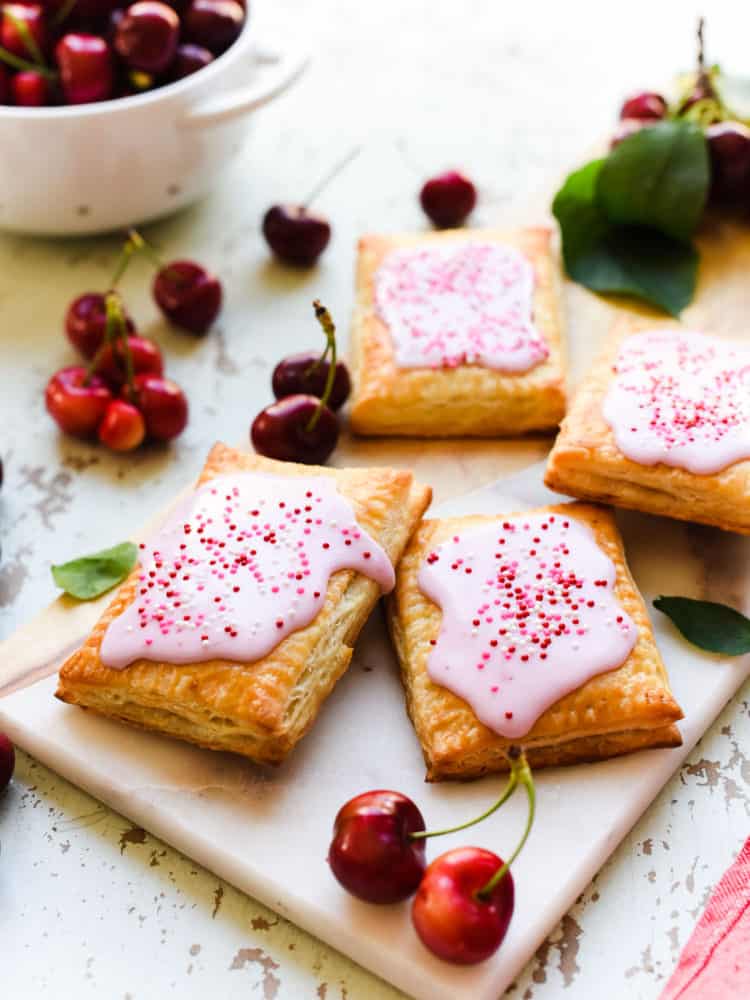 Homemade Cherry Pop Tarts on a wood and marble serving board with fresh cherries.