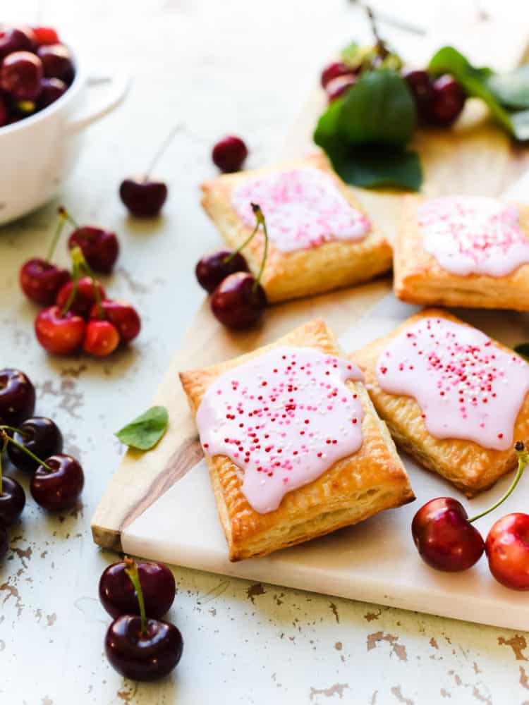 Homemade Cherry Pop Tarts with icing and sprinkles on a wood and marble serving board with fresh cherries.