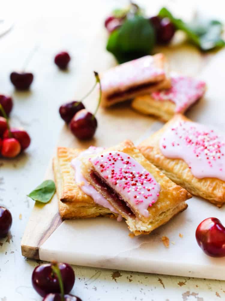 Inside view of Homemade Cherry Pop Tarts stacked on a marble and wood serving board with fresh cherries.