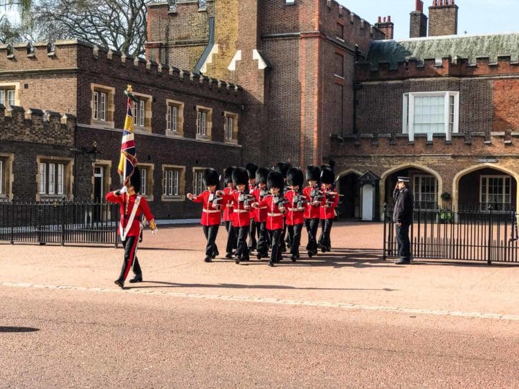 British Royal Guard marching in front of a brick palace.