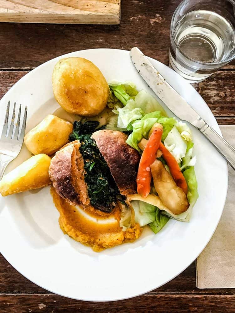 Sunday roast with potatoes, greens, salad, and a roll, served on a white plate.