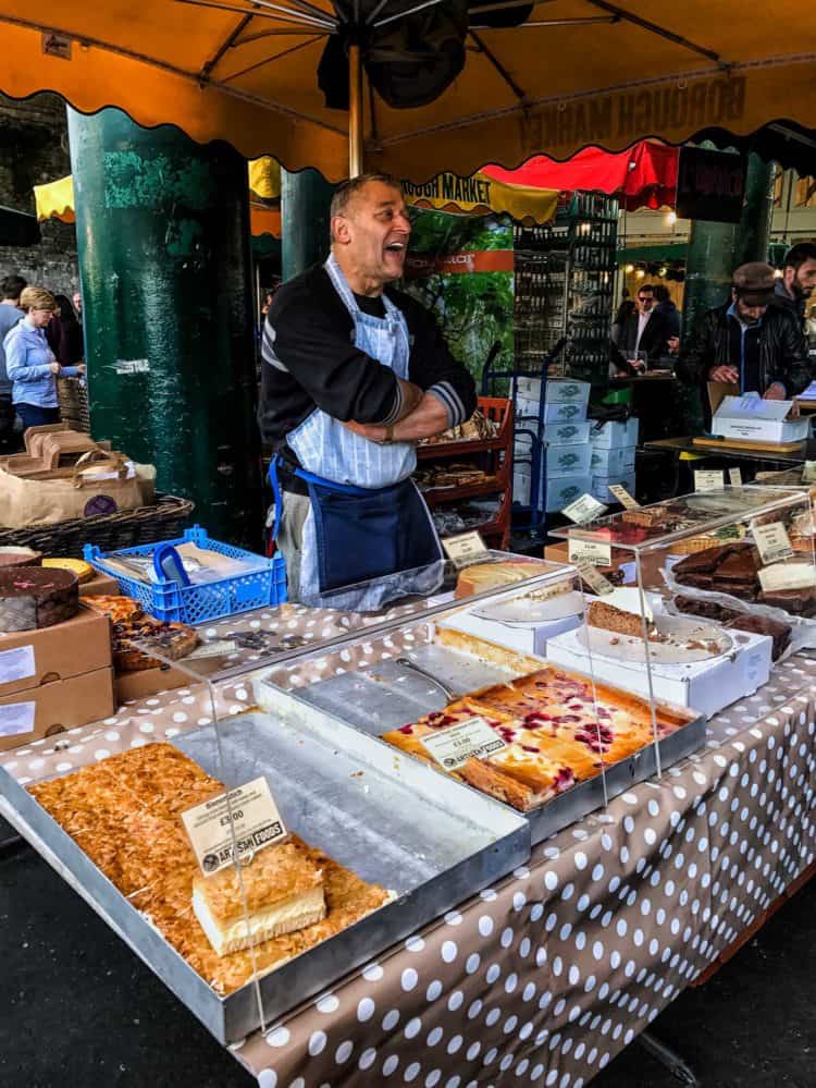 Food stall vendor standing behind pastries at the Borough Market in London.