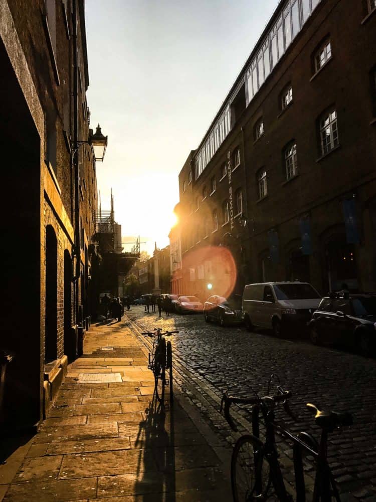 A bike on a cobblestone street, surrounded by brick buildings, at sunset.