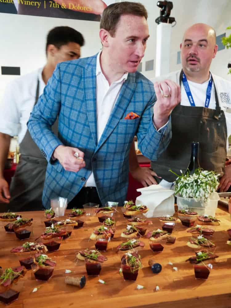 Three men standing behind a wooden table of appetizers at the Pebble Beach Food & Wine.