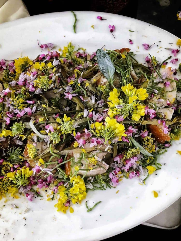 Salad with greens and yellow and purple flowers on a white plate at the Pebble Beach Food & Wine.