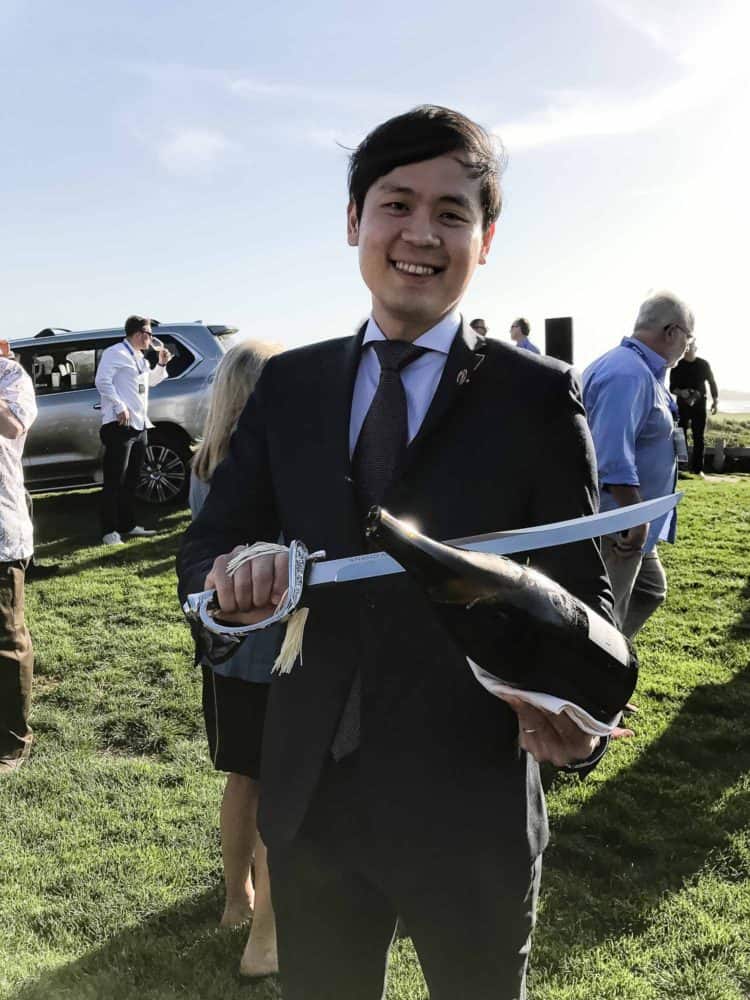 A man in a black suit holding a champagne bottle and saber at the Pebble Beach Food & Wine 2017.
