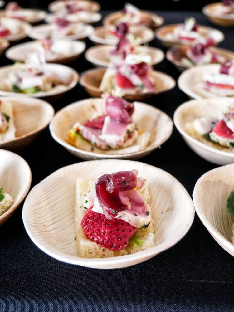 Small wooden bowls holding appetizers containing duck prosciutto and pickled strawberries at the Pebble Beach Food & Wine.