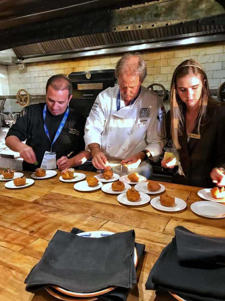 Two men and one woman arranging food on small plates in a professional kitchen at the Pebble Beach Food & Wine.