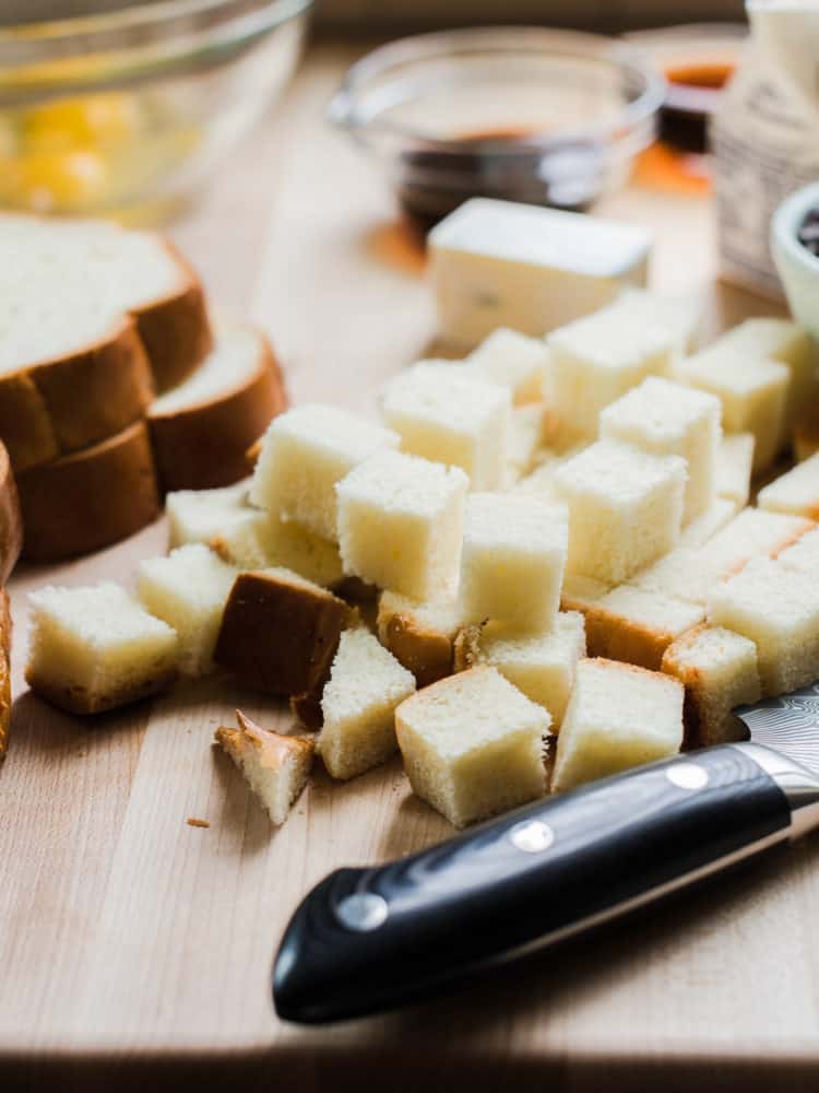 Cubes of bread for bread pudding on a wooden cutting board.