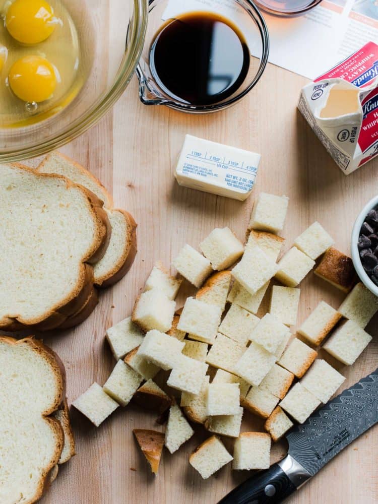 Cubes of bread, butter, and eggs for bread pudding on a wooden cutting board.