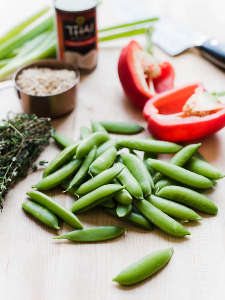 Sugar snap peas, red pepper, barley, and coconut milk on a wooden cutting board.