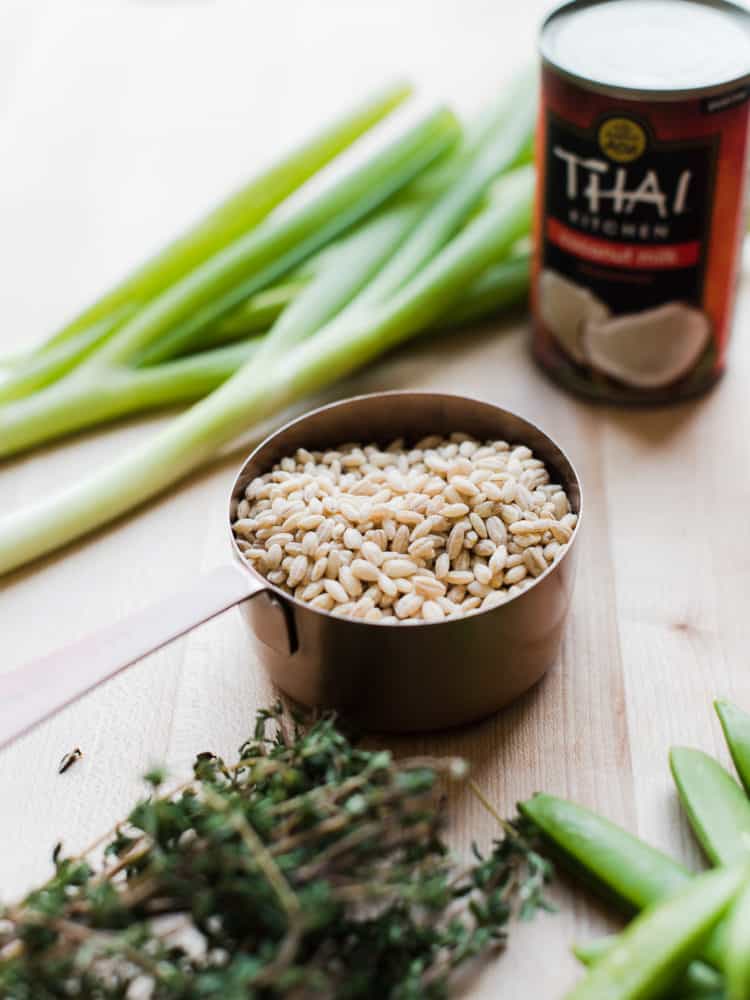 Barley, scallions, and coconut milk on a wooden cutting board.