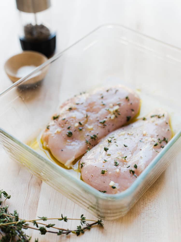 Chicken breasts marinating in a glass dish.