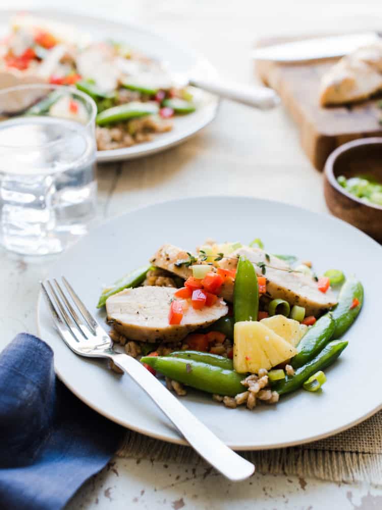 Chicken breast strips, sugar snap peas, and pineapple on a bed of barley, served on a white plate.