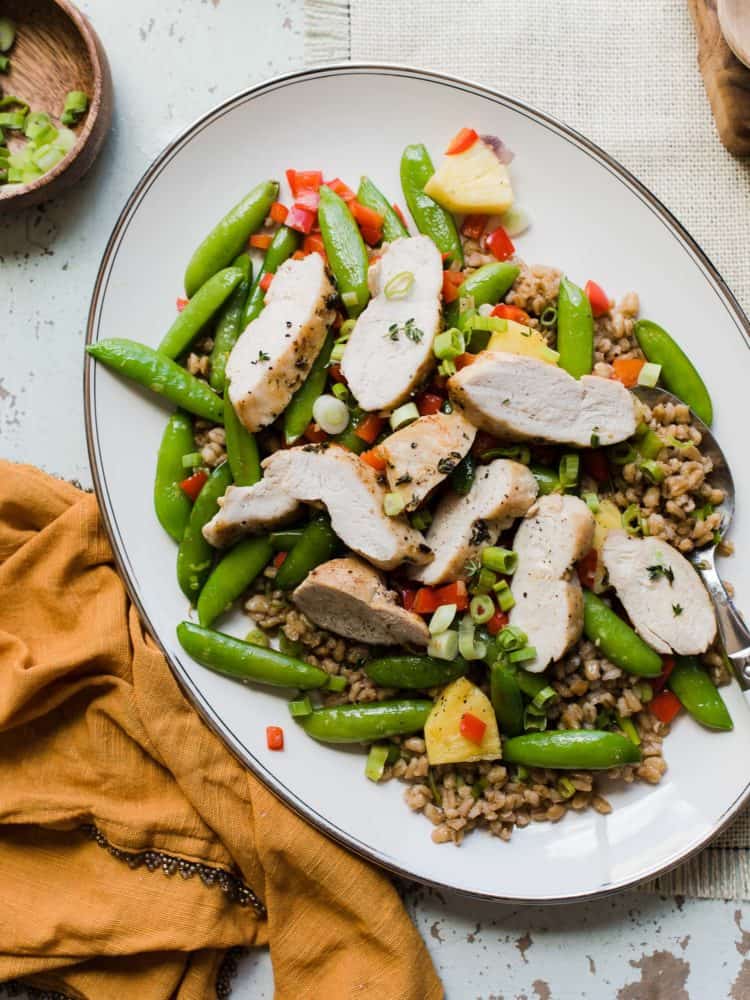 Chicken breast strips, sugar snap peas, and pineapple on a bed of barley, served on a white platter.