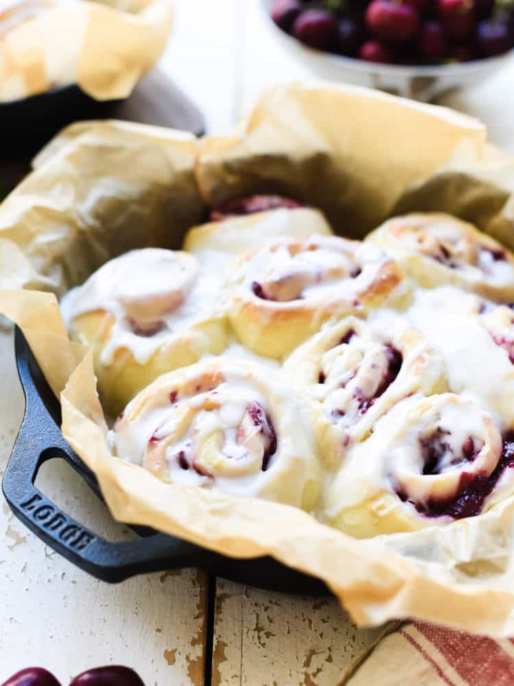 Cherry rolls with icing in a parchment lined cast iron pan.