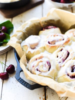 Cherry rolls with icing in a parchment lined cast iron pan.