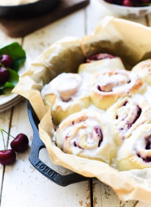 Cherry rolls with icing in a parchment lined cast iron pan.